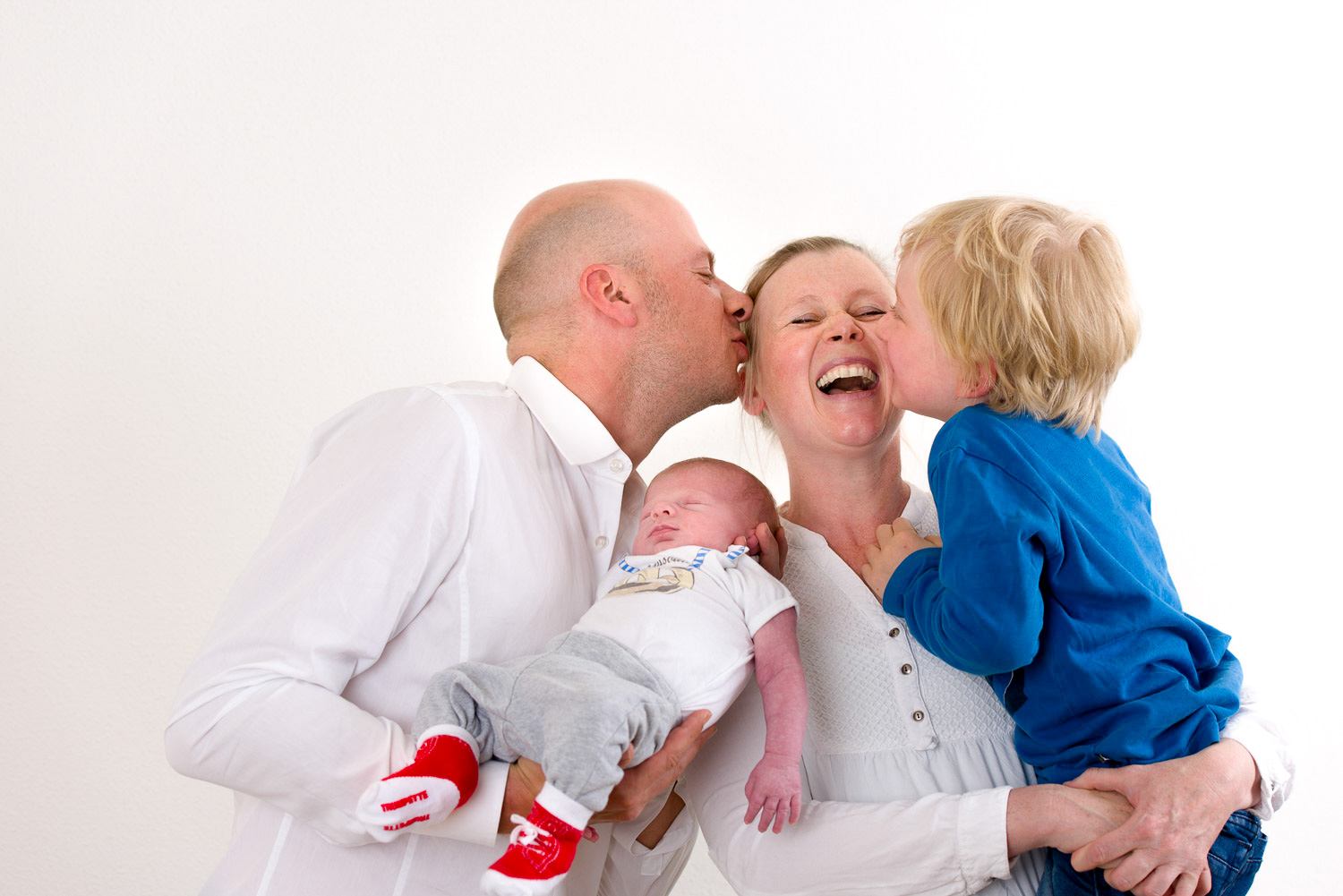 Familienfotografie Erlangen-Shooting Erlangen, Familienfotografie-Kind und Mann küssen die Frau bzw. die Mutter. Mann hat neugeborenes auf dem Arm.