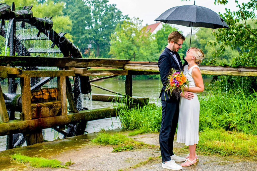 Ein junges Brautpaar steht an einem Wasserrad - Familien- und Hochzeitsfotograf Erlangen 